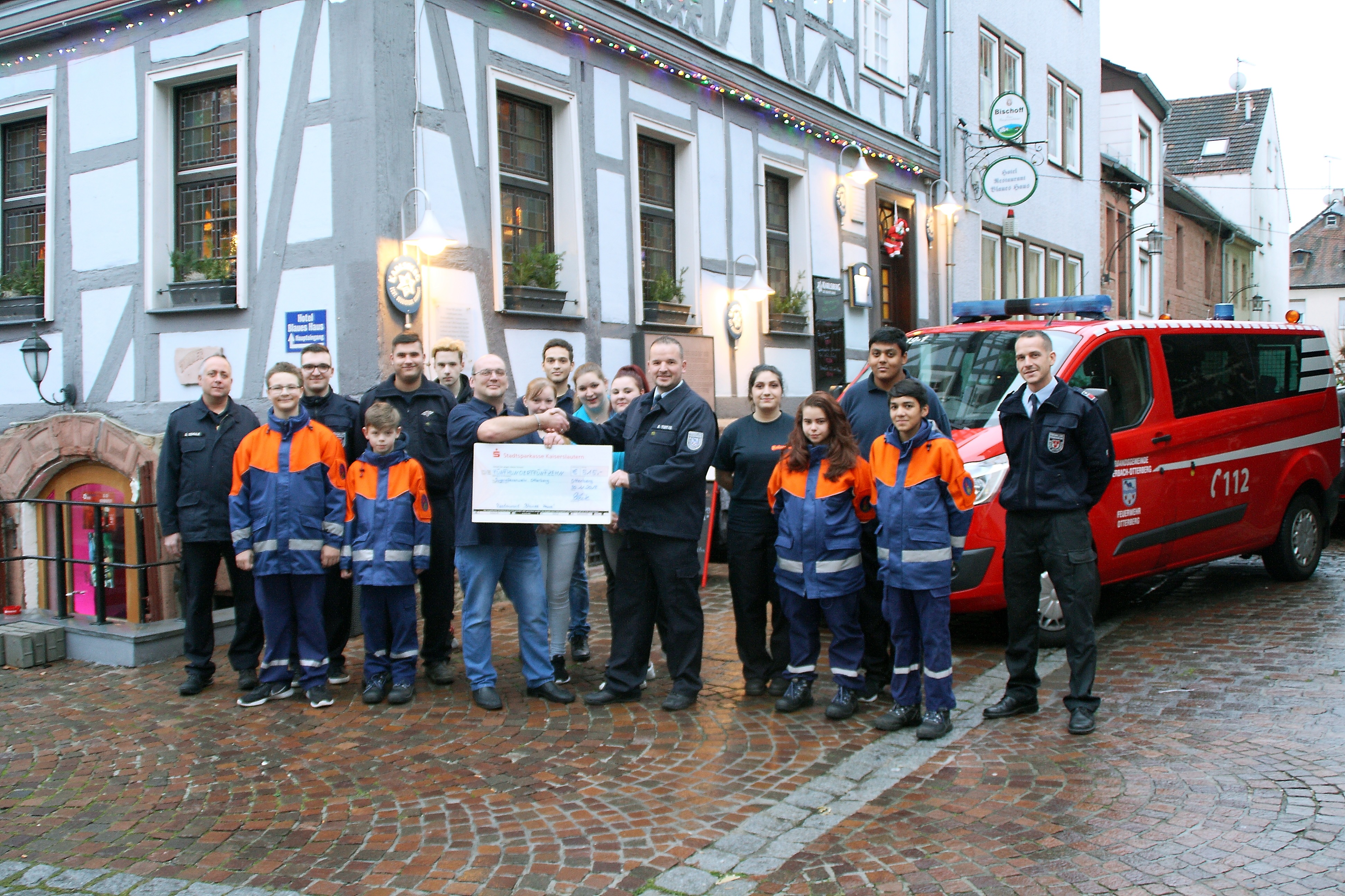 Holger Fleck und Jugendfeuerwehrwart Björn Tietje mit dem symbolischen Scheck, links: stellvertretender Wehrleiter Danny Schulz, rechts: Wehrführer Jörg Tremmel, das Team des Blauen Hauses, Betreuer und Angehörige der Jugendfeuerwehr.