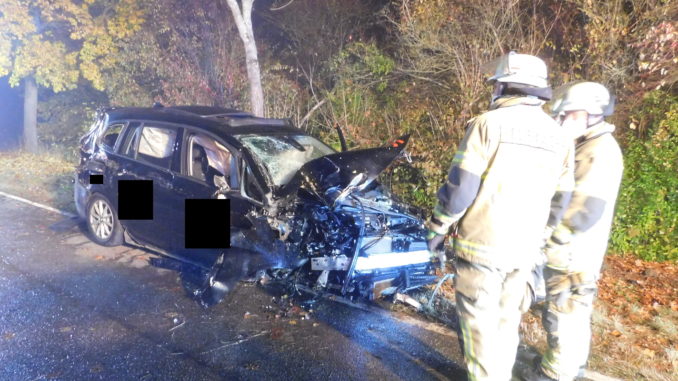 Zwei Feuerwehrangehörige betrachten das Unfallfahrzeug.
