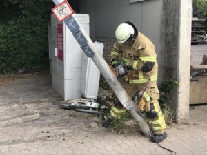 Mit einem Winkelschleifer sägt ein Feuerwehrmann die schräghängende Straßenlaterne um.