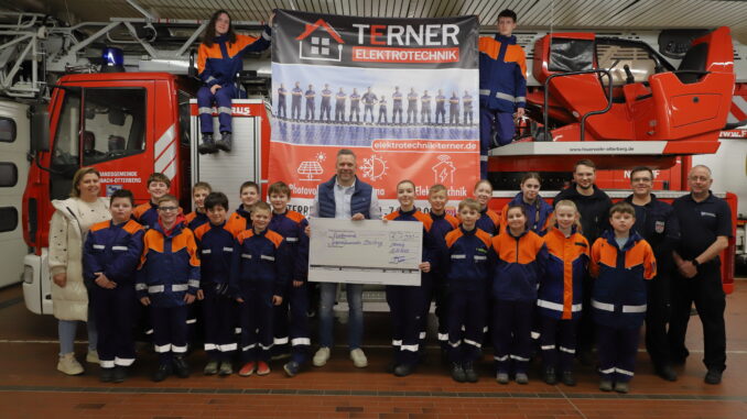 Stefan Terner überreicht Jugendsprecherin Sophia (beide Mitte) einen symbolischen Spendenscheck für die Jugendfeuerwehr Otterberg. Foto: Harald Laier / Feuerwehr